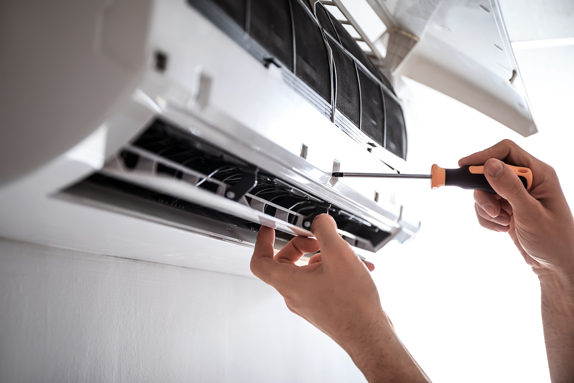Hands using a screwdriver to clean and maintain an air conditioner unit indoors